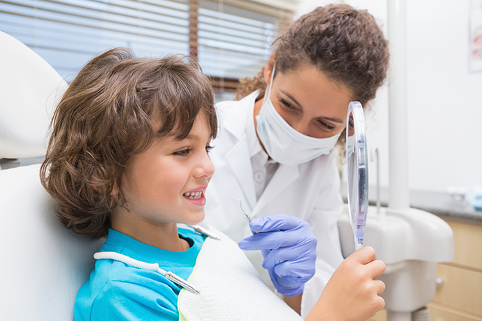 Pediatric dentist showing little boy his teeth in the mirror at the dental clinic